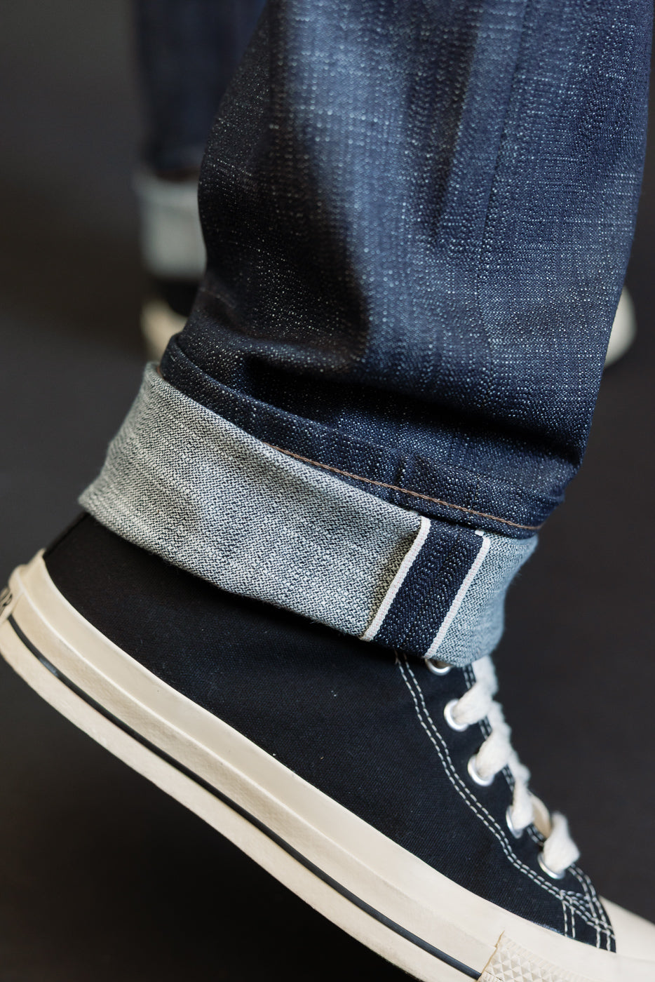 Close-up of the 12.5oz Greencast Stretch Selvedge - Weird Guy jeans, showcasing the cuffed hem with white-pink-white selvedge edge, paired with black canvas sneakers.
