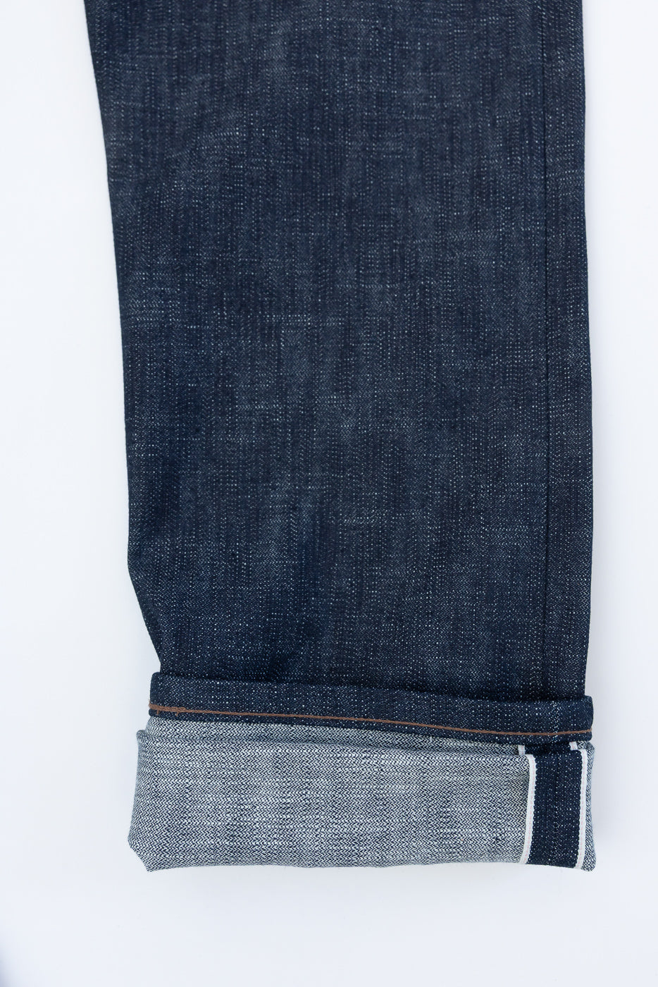 Close-up of the 12.5oz Greencast Stretch Selvedge - Weird Guy jeans, showcasing cuffed hem with white-pink-white selvedge edge, highlighting the denim's rich texture and unique indigo-green cast.