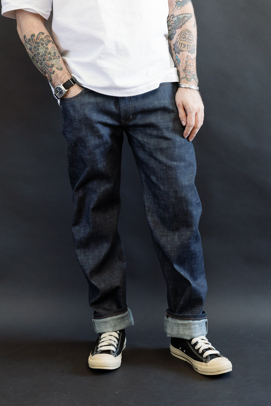 12.5oz Greencast Stretch Selvedge - Weird Guy jeans with wide cuffs, paired with black low-top canvas sneakers and accessories, highlighting the jeans’ detailed texture and indigo rope-dyed green cast.