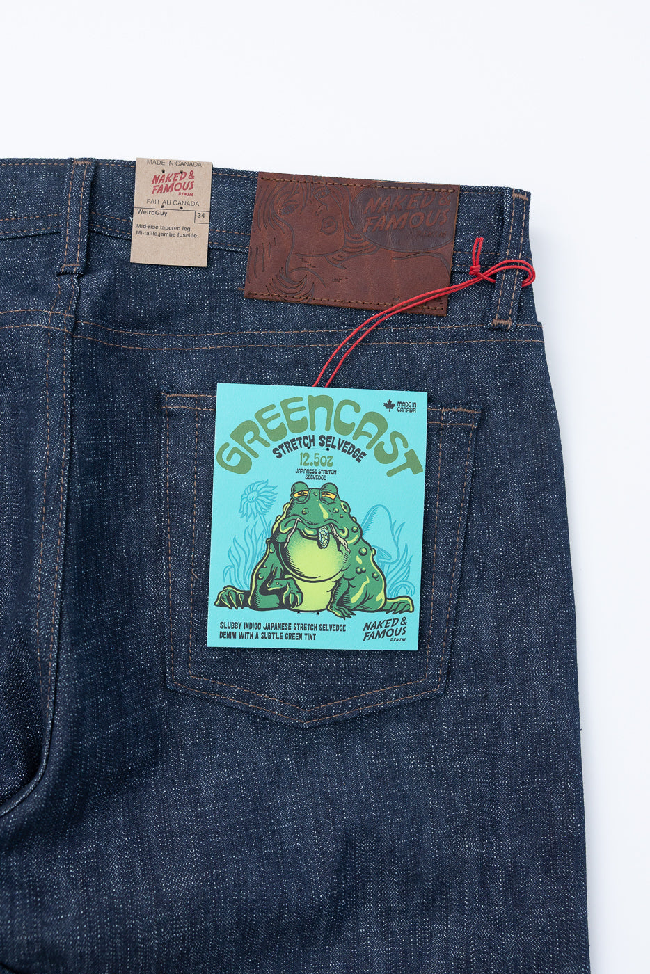 Dark-indigo jeans by Naked & Famous Denim showing the back waistband with a brown leather patch and tags detailing the 12.5oz Greencast Stretch Selvedge - Weird Guy fit, highlighting its unique Japanese denim features.