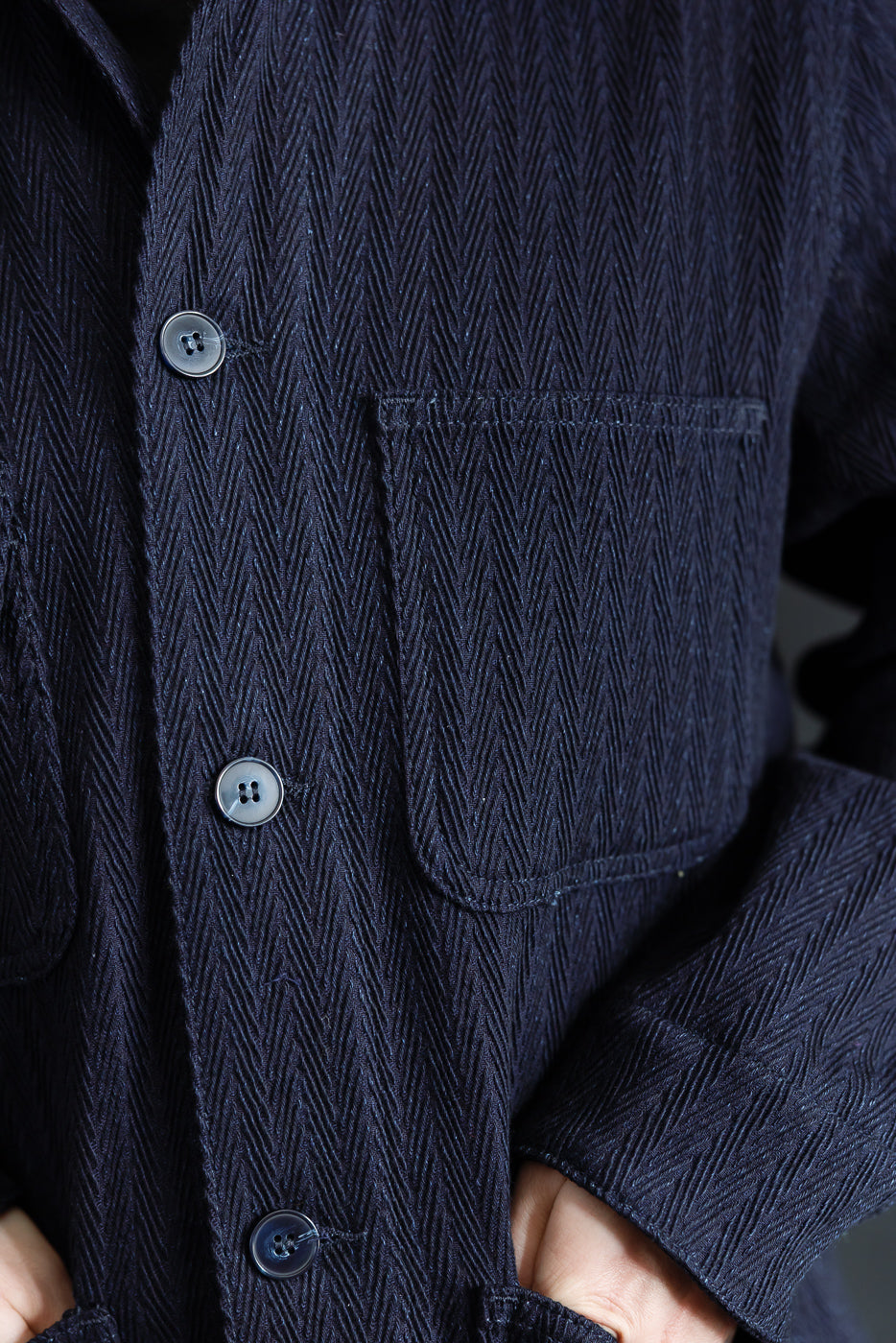 Close-up front view of Naked & Famous indigo chore coat, showing herringbone fabric, buttons, and chest pocket details.