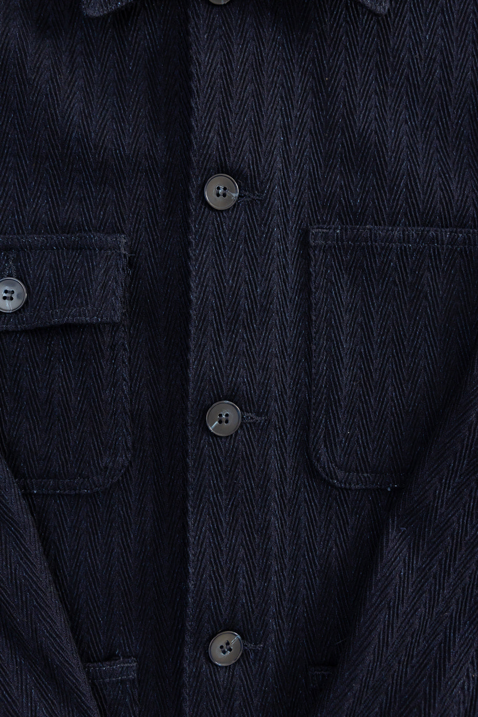 Close-up front view of Naked & Famous indigo chore coat, showing chest pockets, buttons, and textured herringbone fabric.
