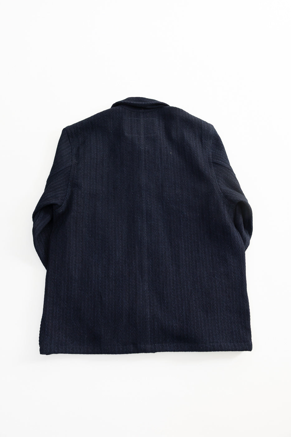Flat lay of Naked & Famous 12oz indigo Sugiaya chore coat, back view, showing textured denim