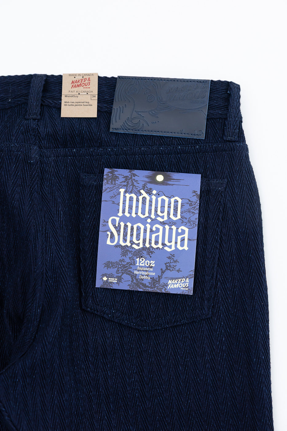 Close-up of back waist detail on Naked & Famous Indigo Sugiaya 12oz herringbone jeans, showing tags and textured selvedge fabric.
