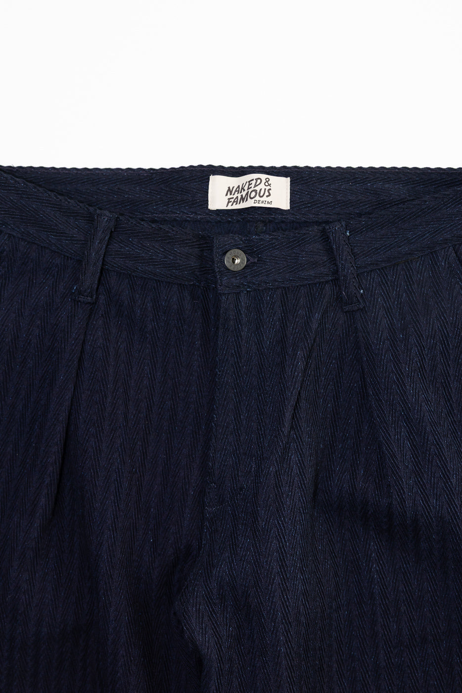 Close-up of front waistband and button detail on Naked & Famous indigo pleated trouser