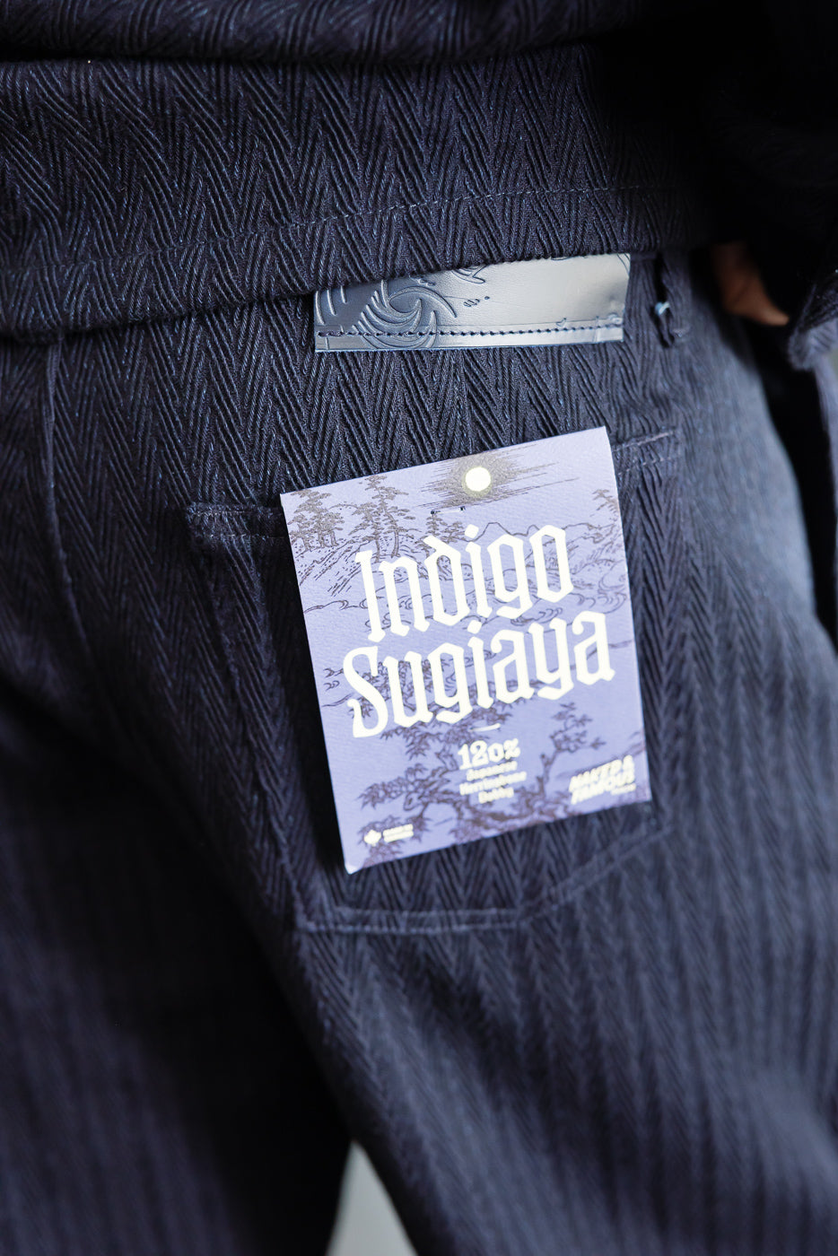 Close-up of back of Naked & Famous Indigo Sugiaya pleated trouser, herringbone texture, tag visible.