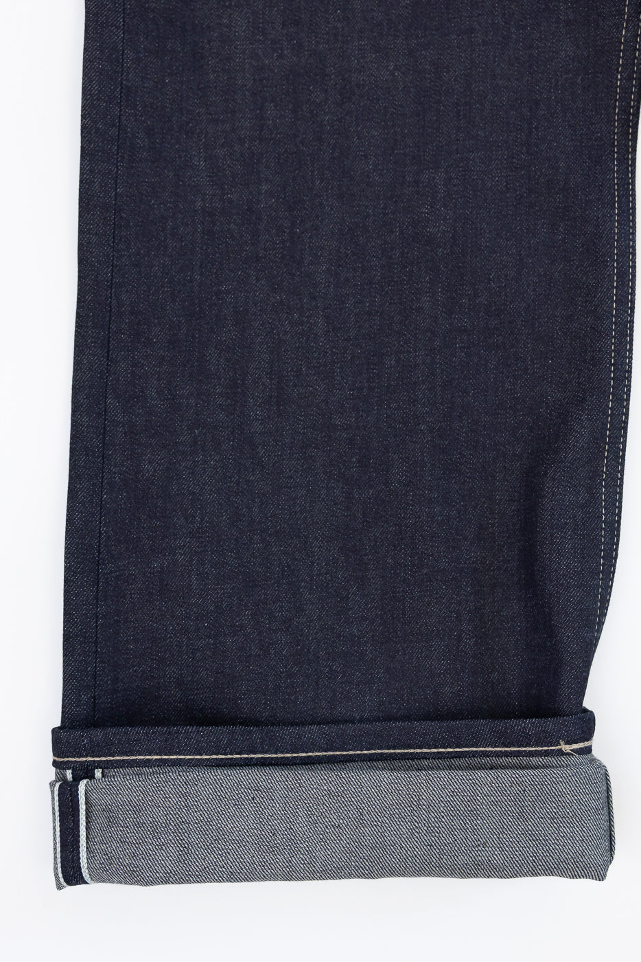 Close-up of the bottom hem and cuffed selvedge detail on dark indigo denim jeans, front view.
