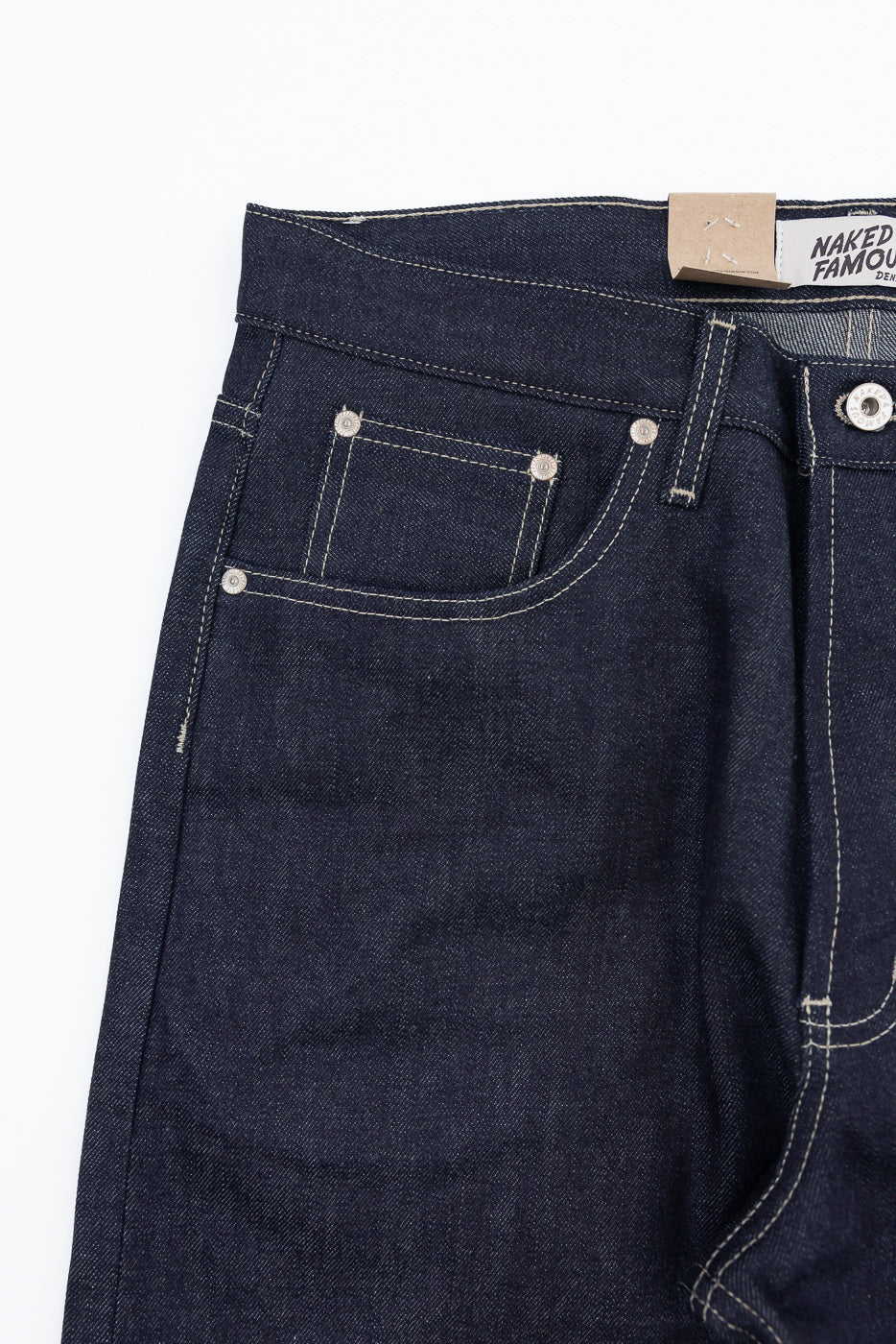 Close-up of the front right hip of dark blue selvedge denim jeans with a Naked & Famous tag.