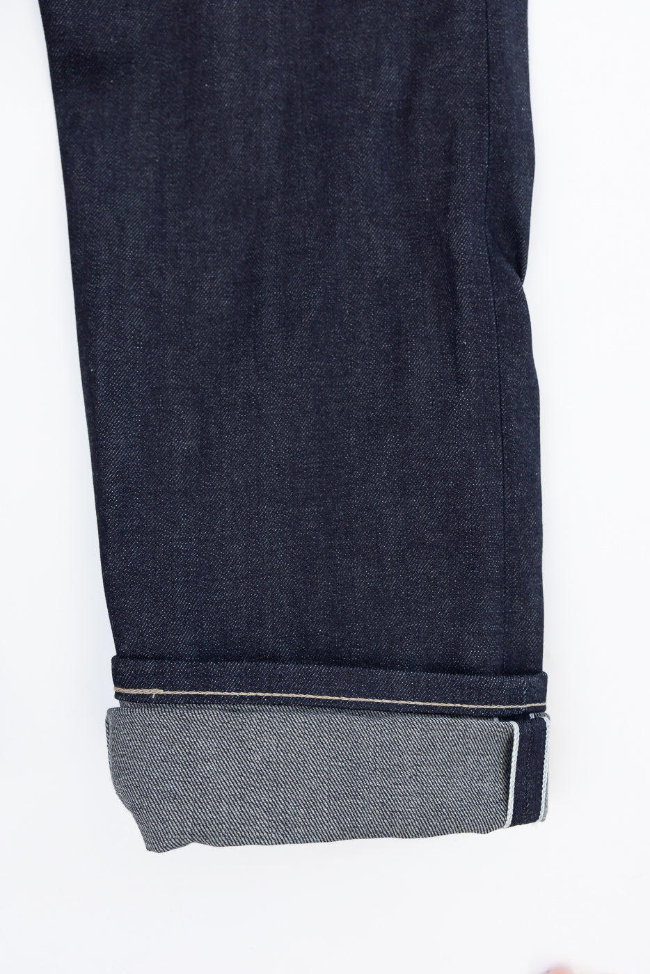 Close-up of the bottom hem and selvedge cuff of dark indigo denim jeans, front view.
