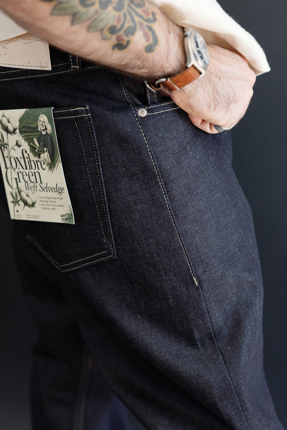 Close-up side view of dark indigo selvedge denim jeans on a male model, showing back pocket.
