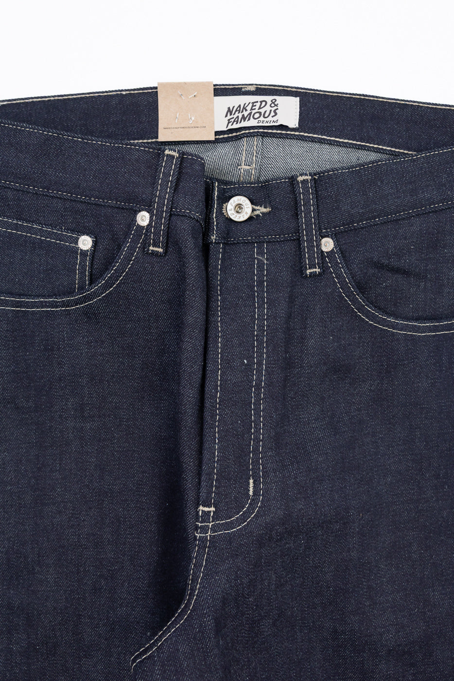 Close-up of the front waist and fly of Naked & Famous Denim jeans showing tag and button.