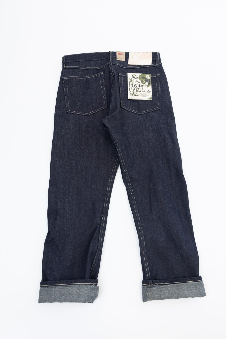 Back view flat lay of dark blue selvedge denim jeans featuring a white back pocket patch.