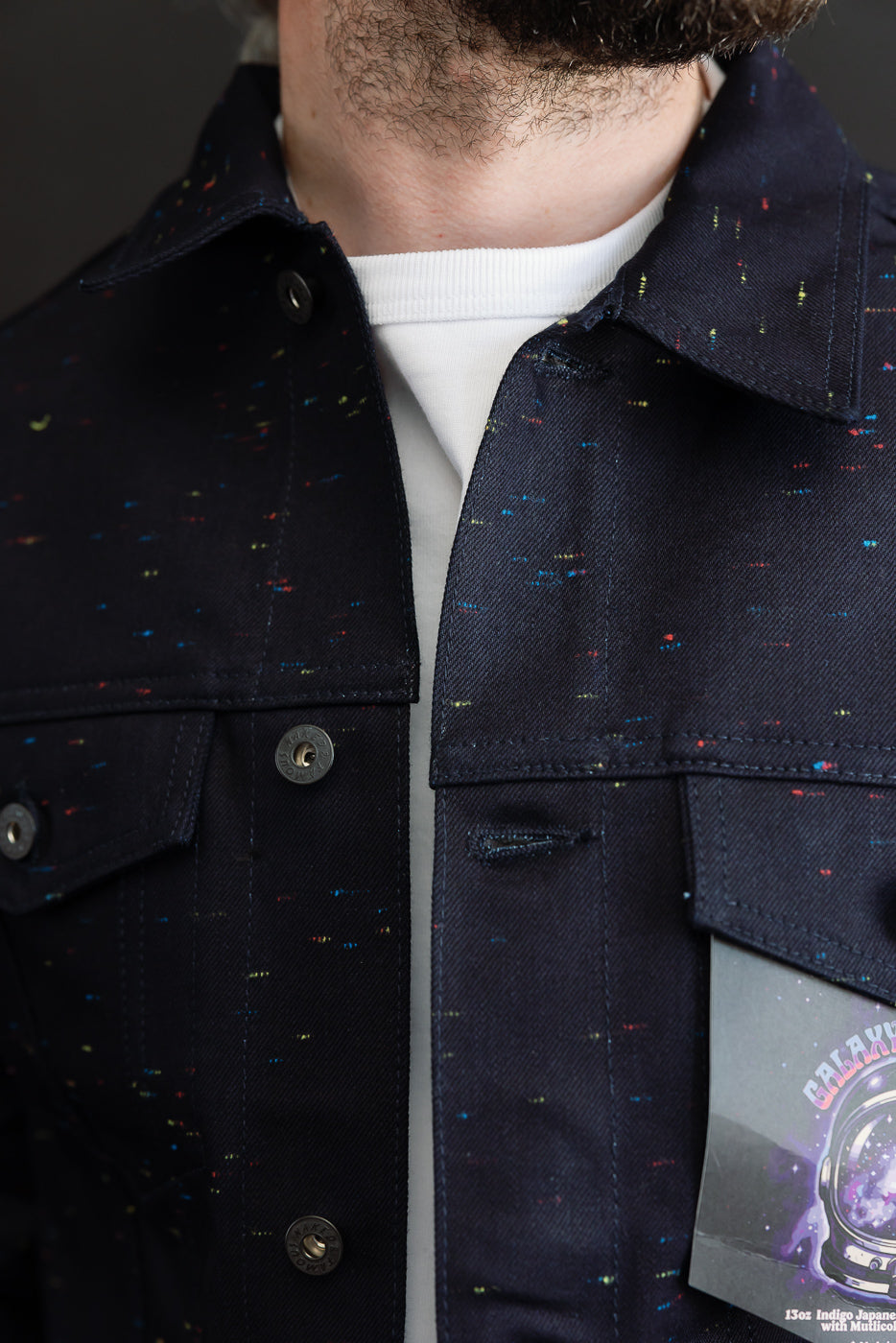 Close-up front view of a male model wearing a dark navy multicolor speckled denim jacket.