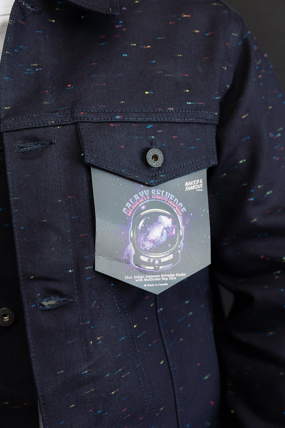 Close-up front view of a dark indigo denim jacket featuring multicolor nep yarn texture and a chest pocket with a Galaxy Selvedge tag.