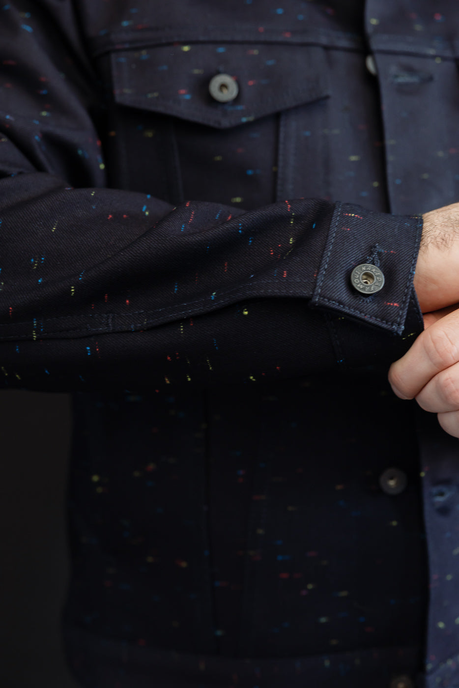 Close-up of a male model's left sleeve cuff and button on a navy patterned jacket.