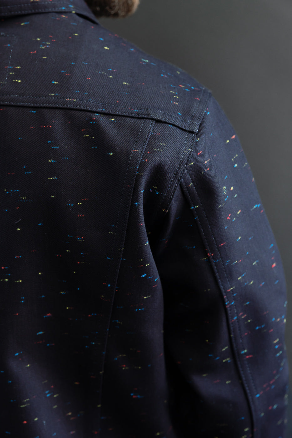 Close-up back view of a navy blue speckled fabric jacket showing shoulder seam and texture.