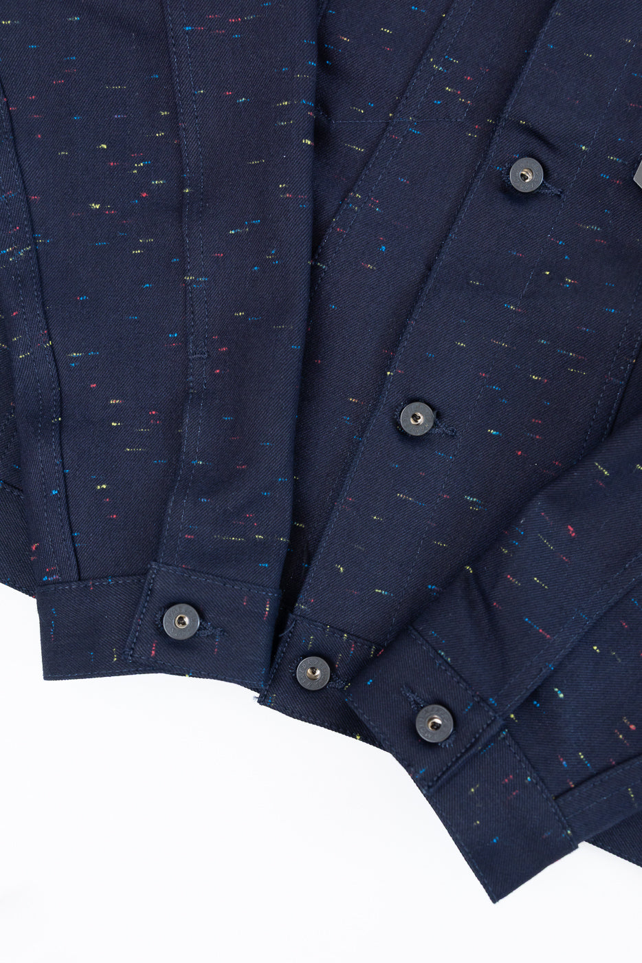 Close-up front view of navy blue textured fabric with colorful speckles and dark buttons.