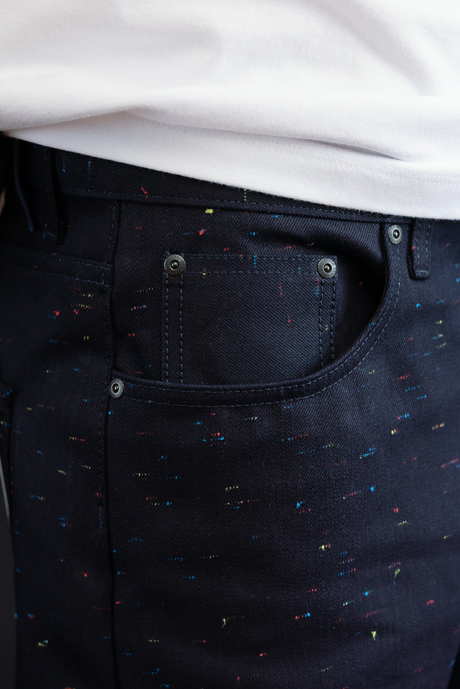 Close-up of the front right pocket and waistband of dark navy speckled denim trousers.