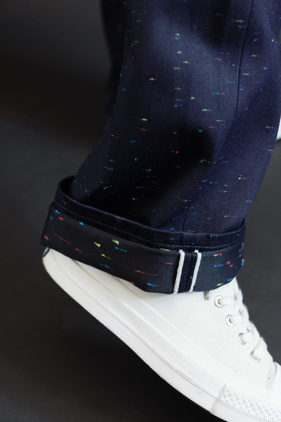 Close-up of the cuffed hem and fabric texture of navy patterned trousers worn with white sneakers.