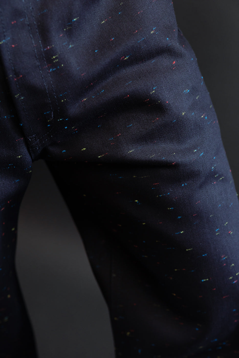 Close-up of the fabric texture and colorful speckle pattern on the side of navy trousers.
