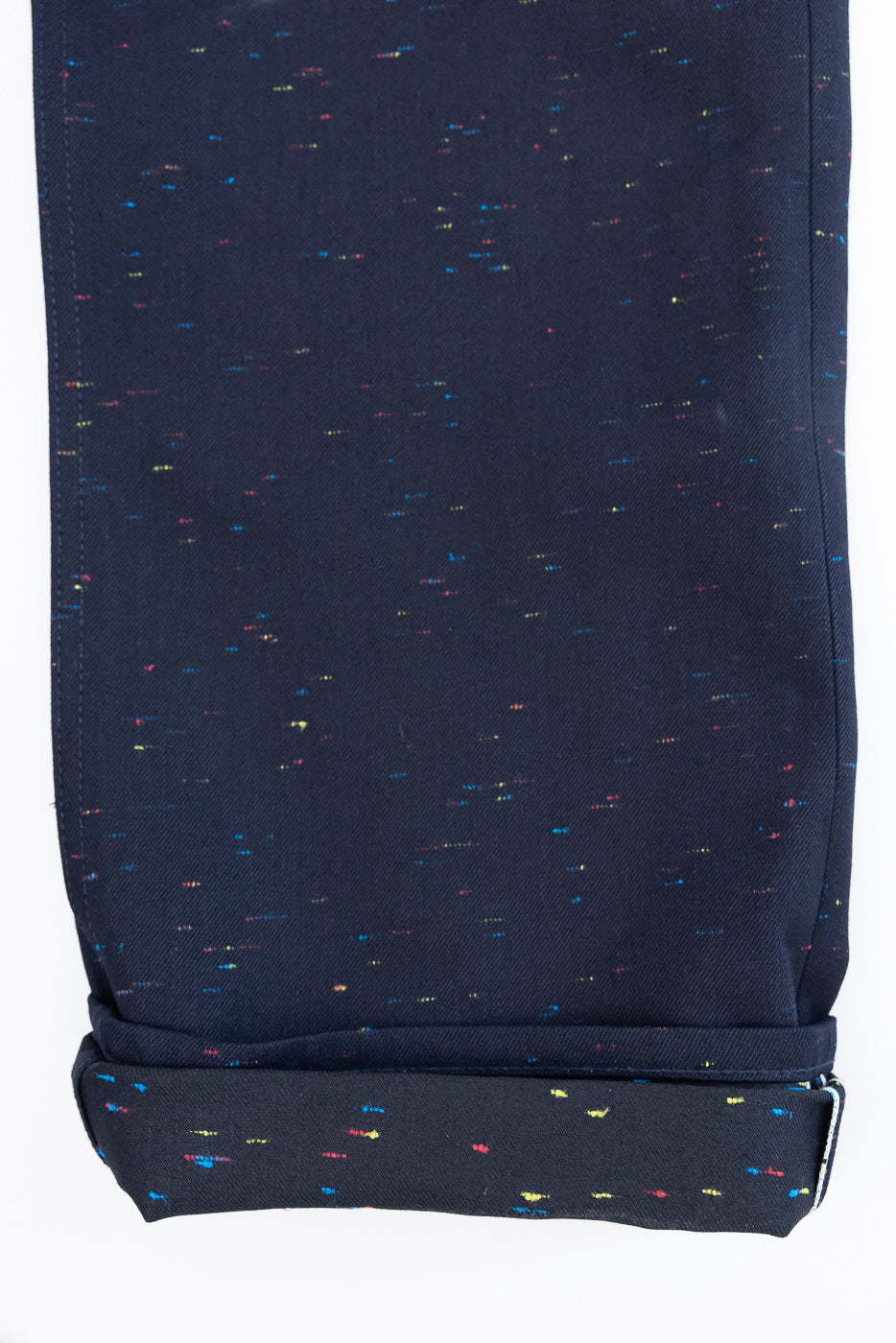 Close-up of the bottom hem and rolled cuff of navy blue speckled fabric trousers.