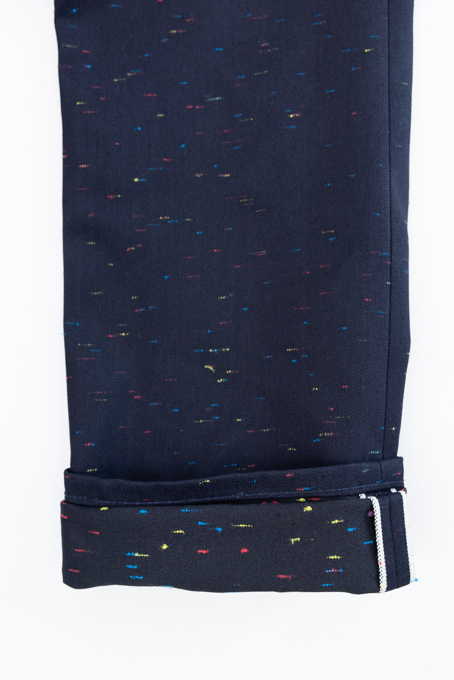 Close-up of the bottom hem and cuffed leg of dark navy speckled trousers, showing selvedge detail.