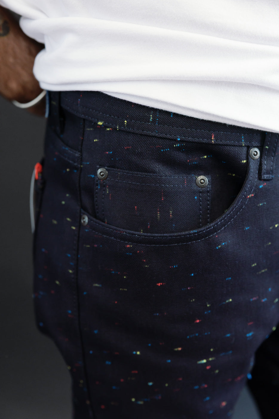 Close-up side view of the back pocket and waistband on dark navy speckled denim pants worn by a male model.