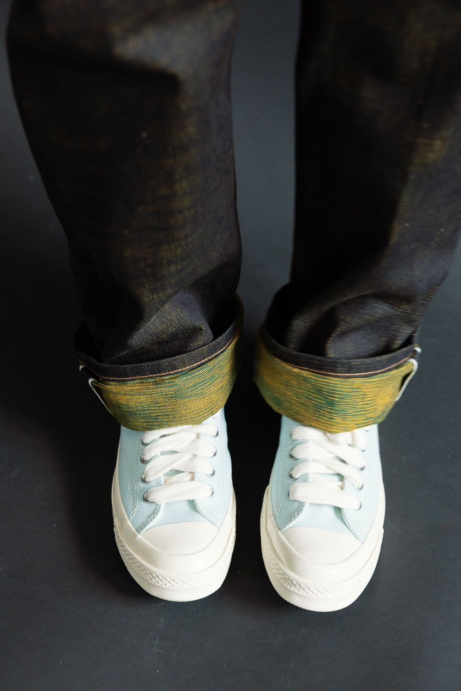 Close-up of men's selvedge denim jeans cuffed at ankle, front view, showing colorful selvedge and light blue sneakers, model is male, 5'9