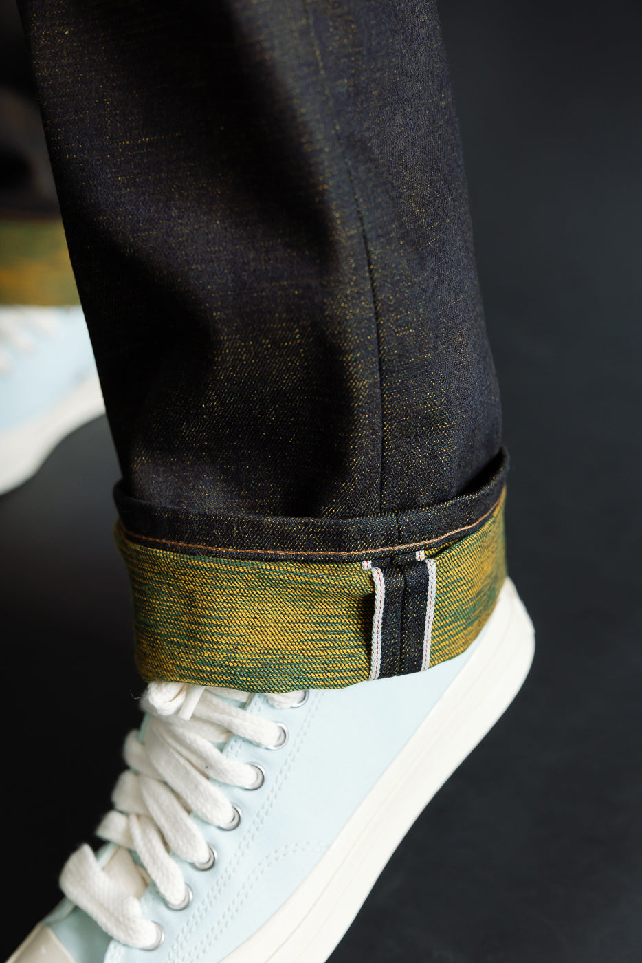 Close-up of a male model’s cuffed jean hem, showing selvedge edge and textured denim, lower leg side view. Model is 5'9