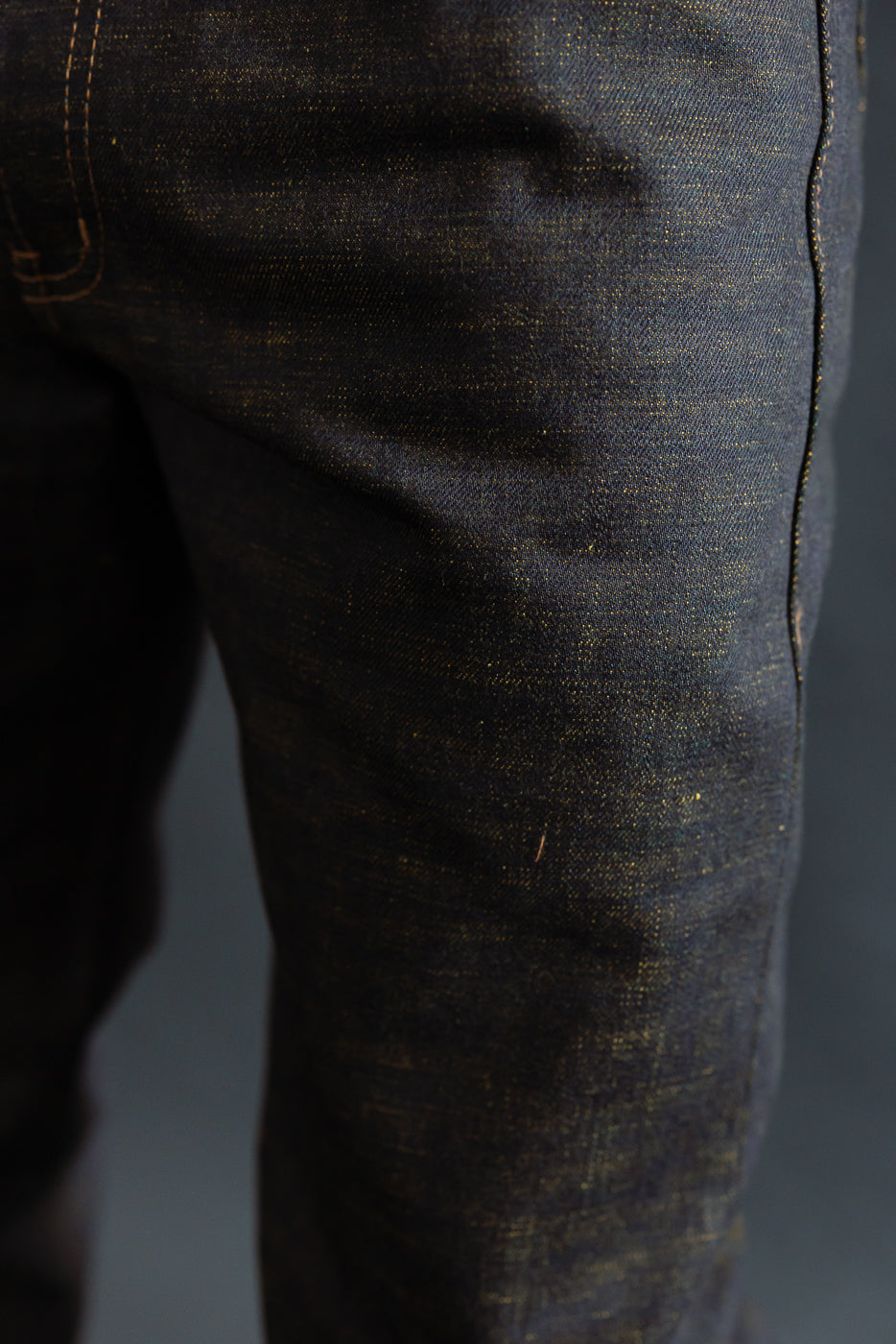 Close-up of men's selvedge denim jeans on male model's left thigh, showing texture and stitching.