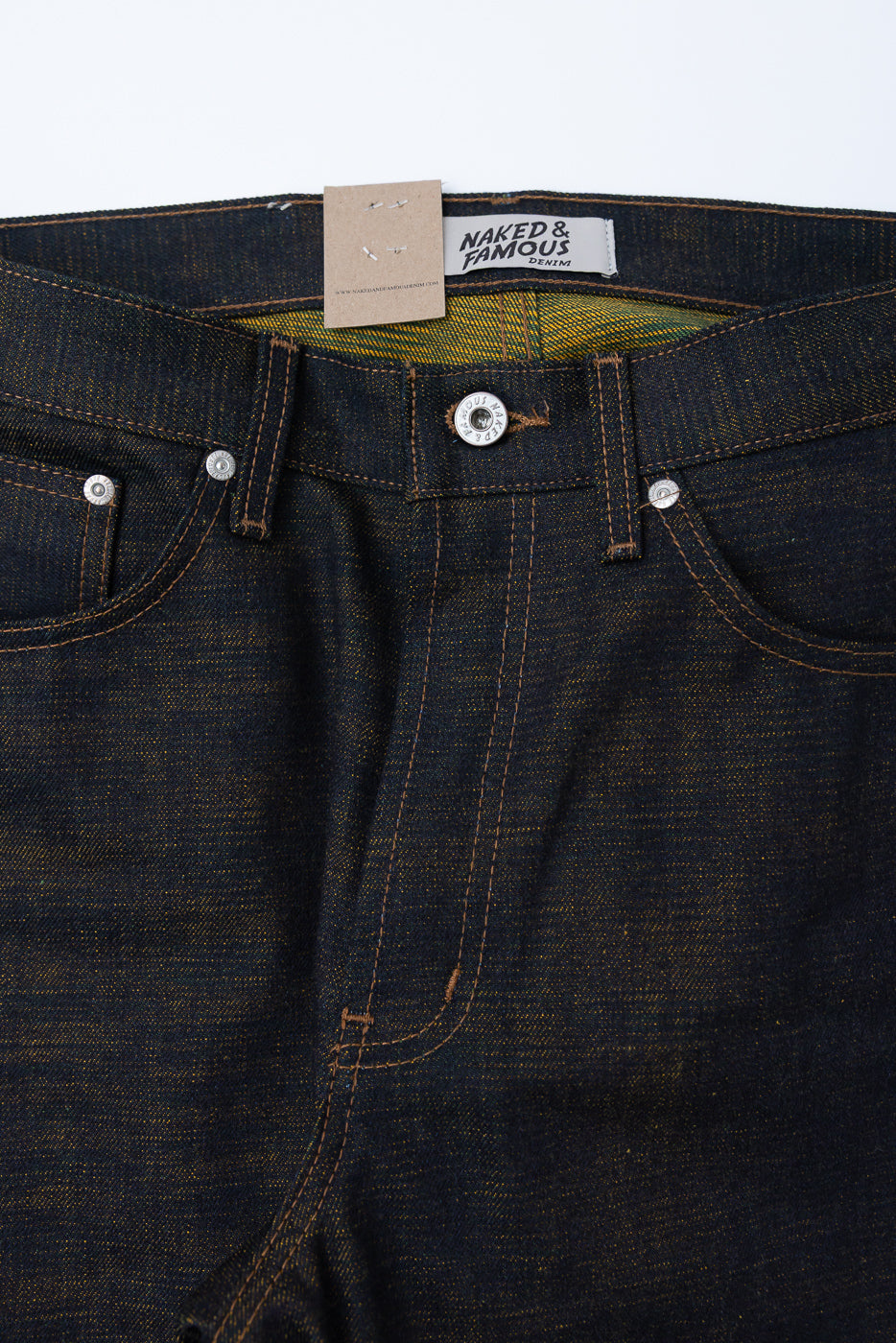 Close-up front view of dark indigo selvedge denim jeans, showing waistband, button, and pockets.