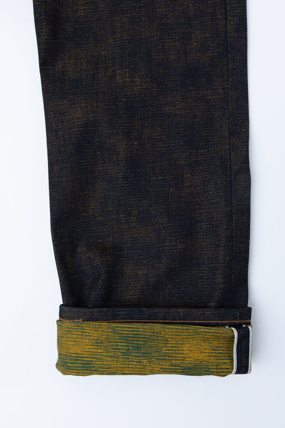 Close-up of cuffed denim pant leg, showing selvedge and textured citrus yellow interior, side view.