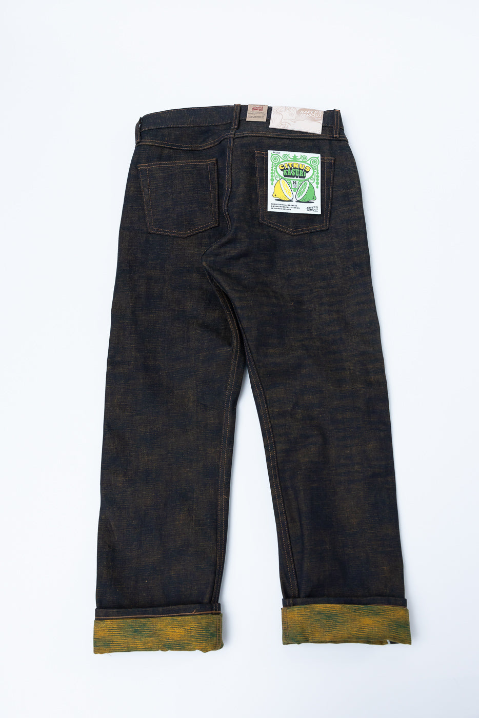 Flat lay of men's selvedge denim jeans, back view showing rear pockets, leather patch, and unique rolled cuffs with colorful inner fabric.