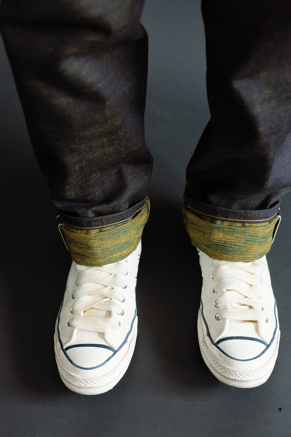 Close-up of male model's cuffed selvedge jeans showing unique green-yellow weft, lower leg view, 5'9