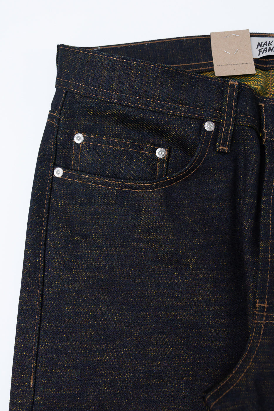 Close-up of front left hip and pocket on dark selvedge denim jeans, showing coin pocket, rivets, and texture detail.