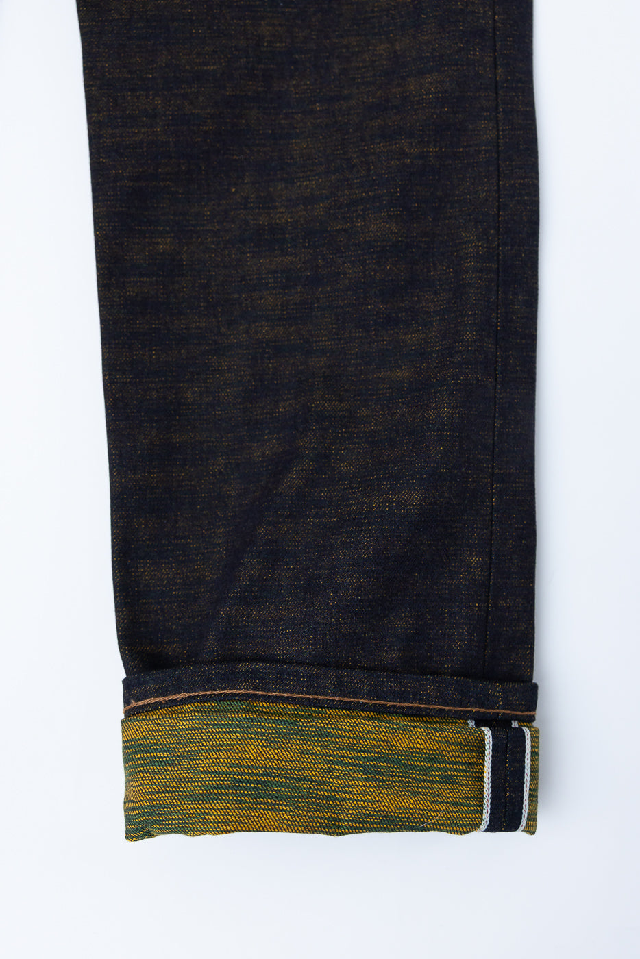 Close-up of jeans leg hem, showing selvedge edge and yellow-green interior fabric, side view.