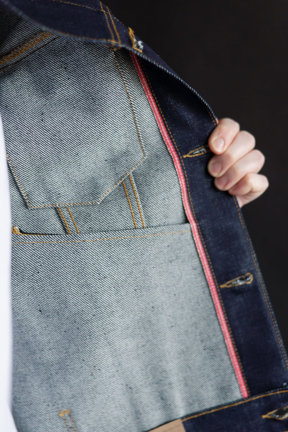 Close-up of inside front left panel of selvedge denim jacket, showing red edge and pocket stitching.