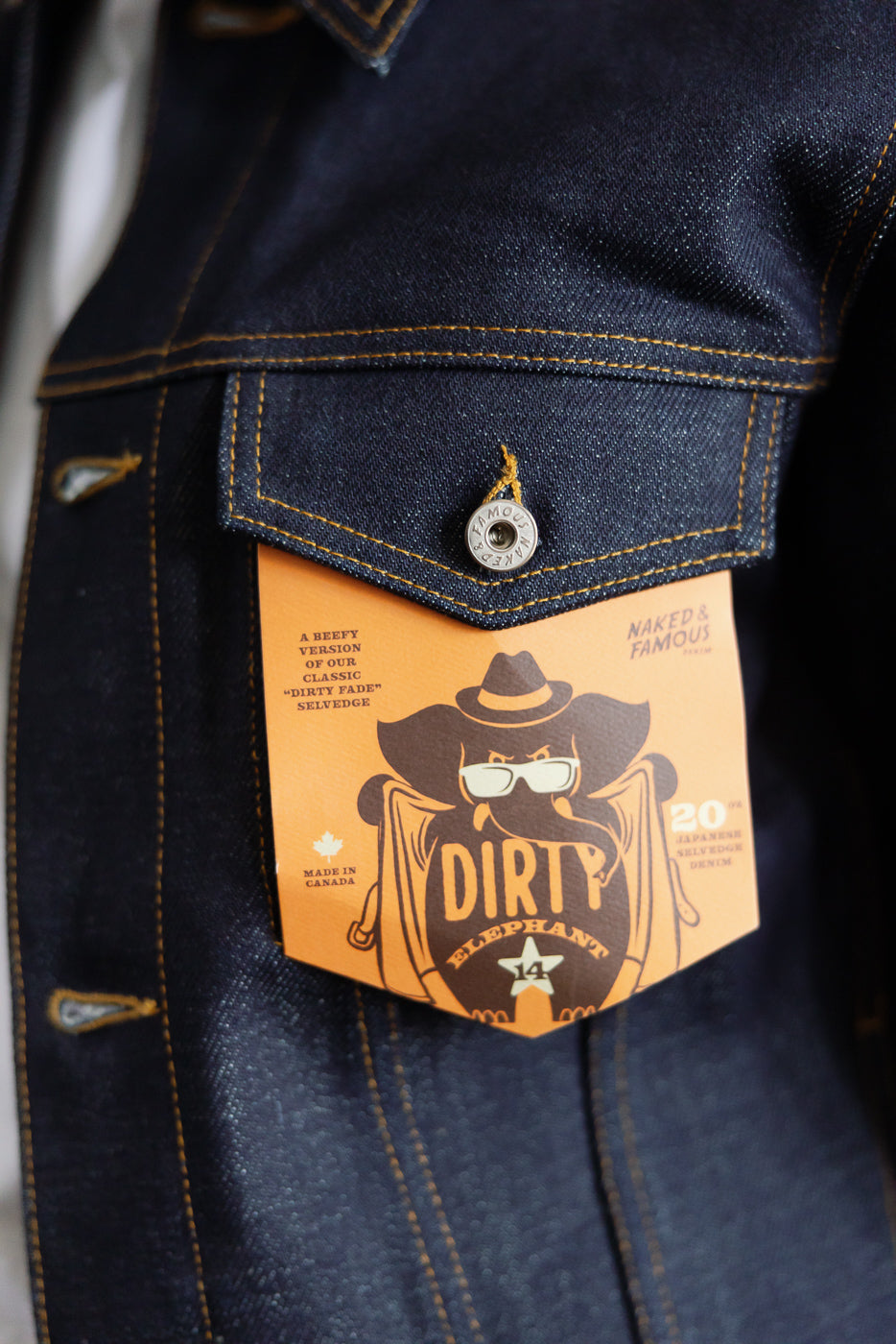 Close-up of front chest pocket on Naked & Famous 20oz Dirty Elephant 14 selvedge denim jacket, showing branded button and tag details.