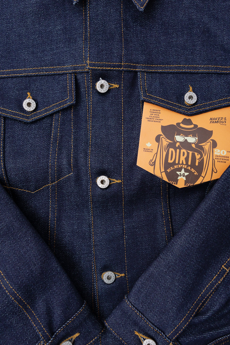 Close-up front of Naked & Famous 20oz Dirty Elephant selvedge denim jacket chest pockets, tag, metal buttons, and contrast stitching, contemporary men's apparel at Dant.