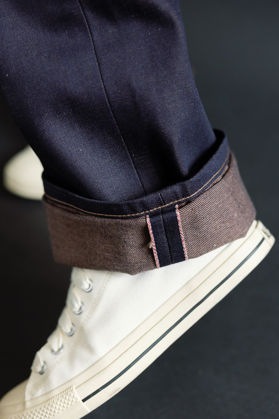 Close-up of male model's cuffed selvedge denim pant leg, showing side hem and selvedge ID.