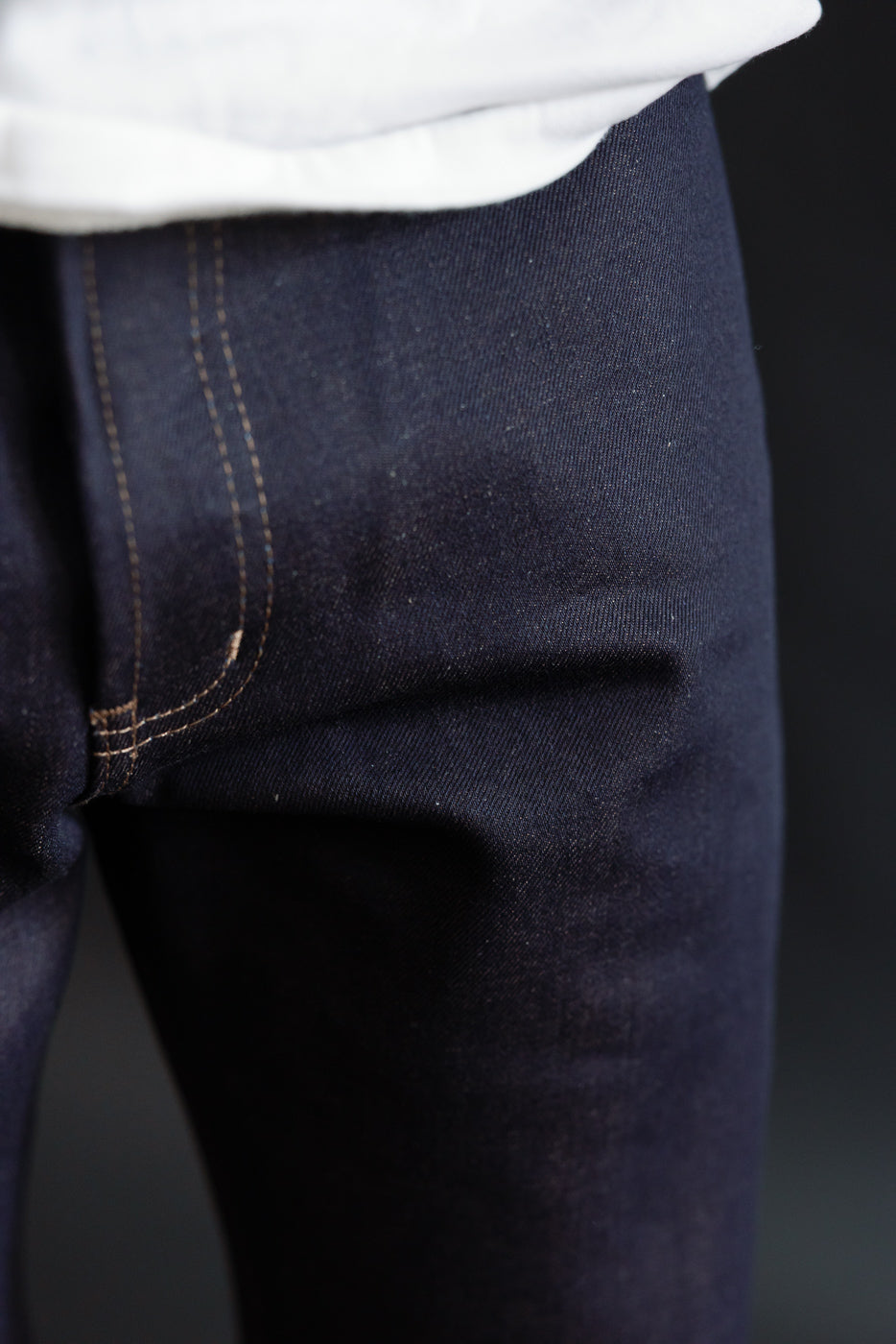 Close-up front view of men's selvedge denim jeans upper thigh, dark indigo, contrast stitching, on male model 5'9