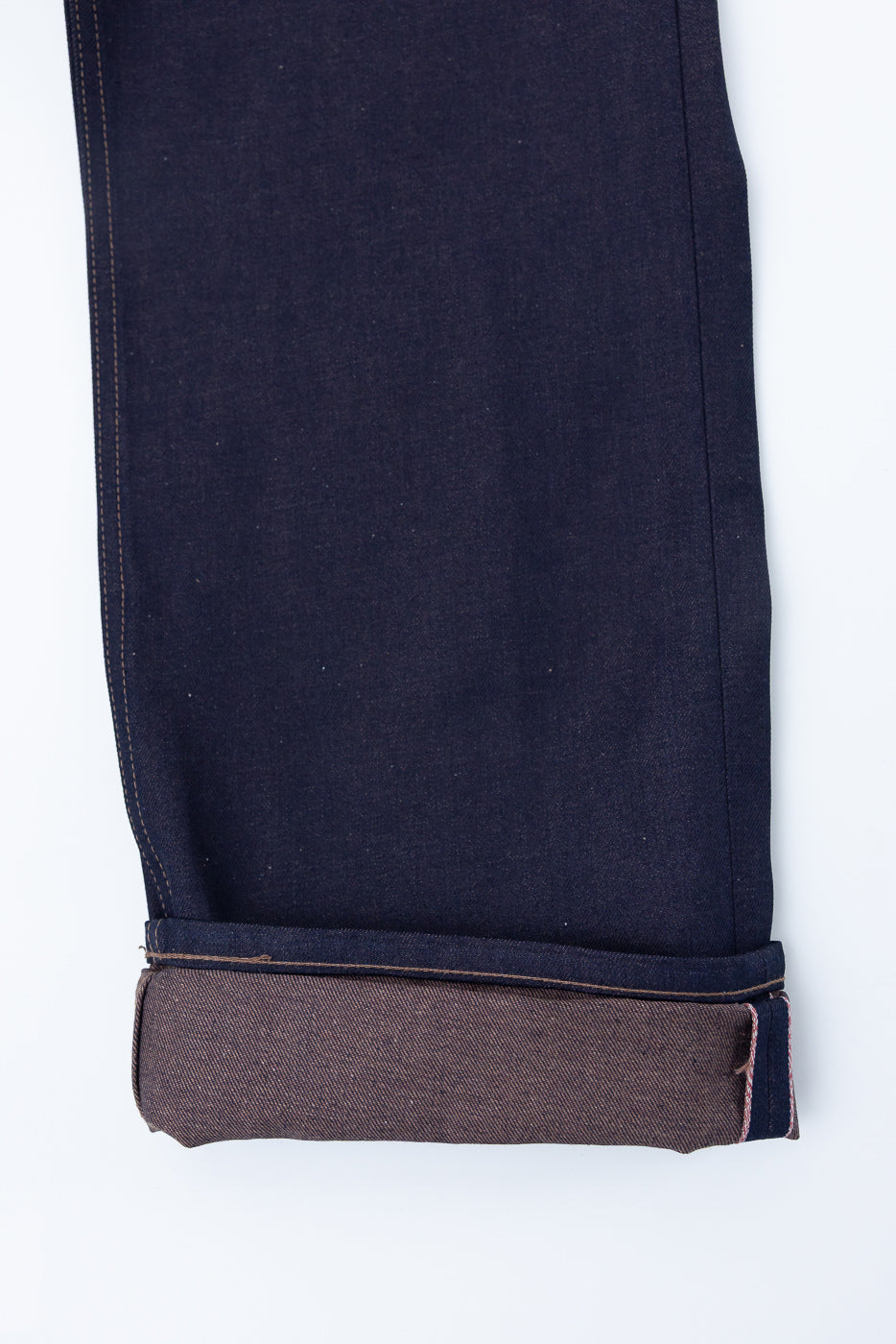 Close-up of the front lower leg and cuff of dark selvedge denim jeans, showing brown weft and visible selvedge ID.