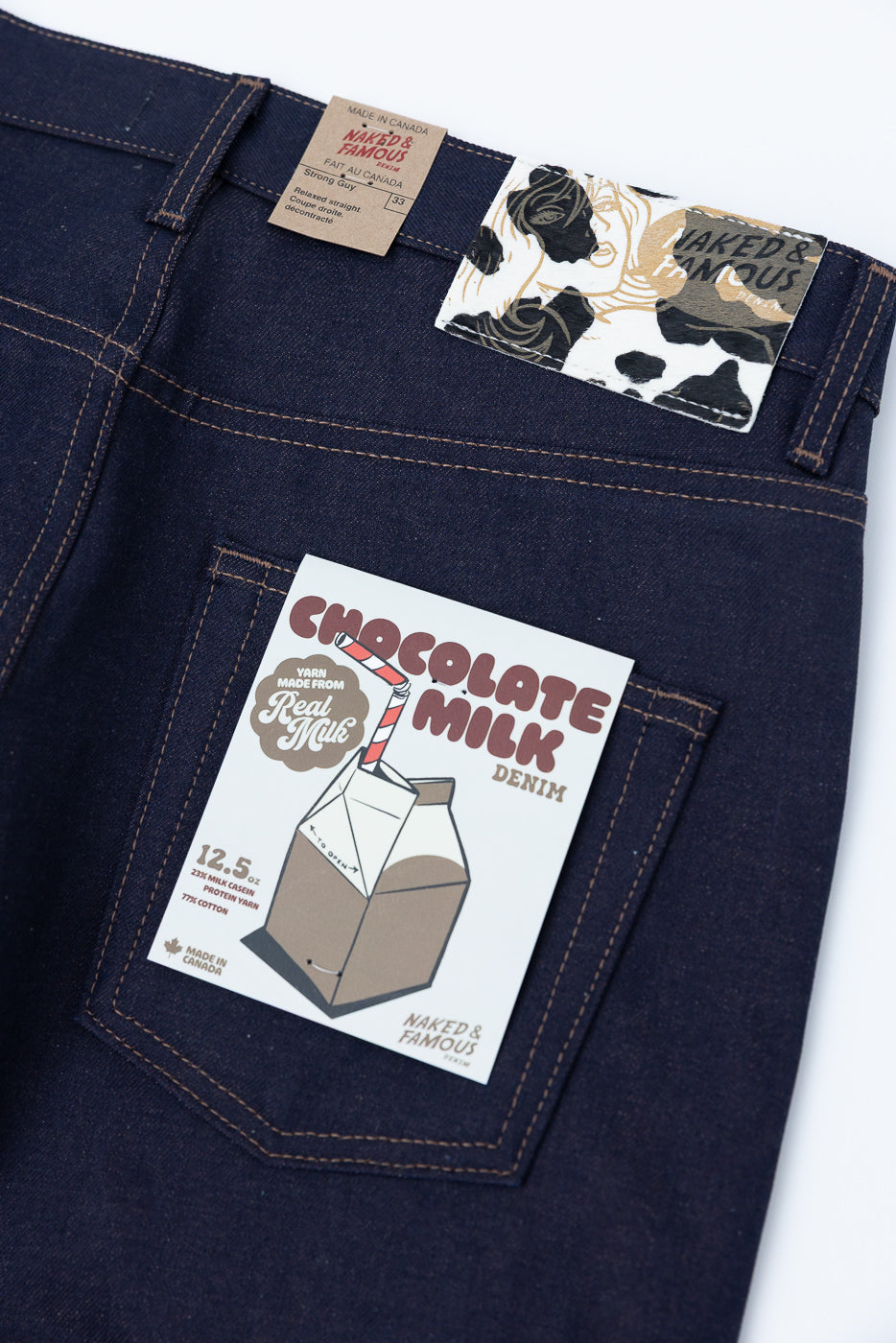 Close-up of back of dark selvedge jeans showing paper tags, back pocket, and leather brand patch.