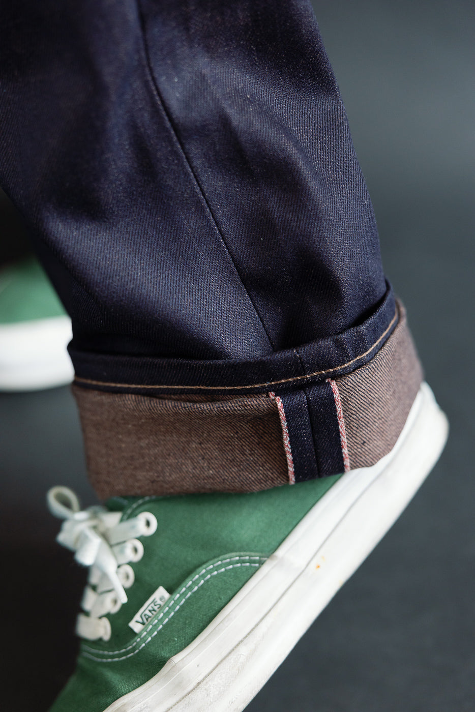 Close-up of men's selvedge denim cuff with brown weft and visible pink stitching, lower leg side view.