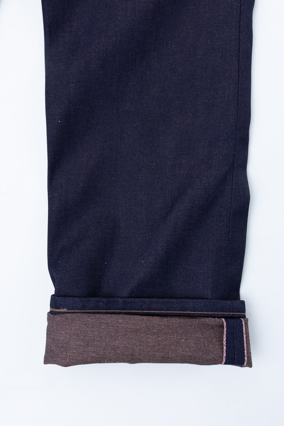 Close-up of cuffed selvedge denim jean leg, showing brown weft and pink edge stitching.