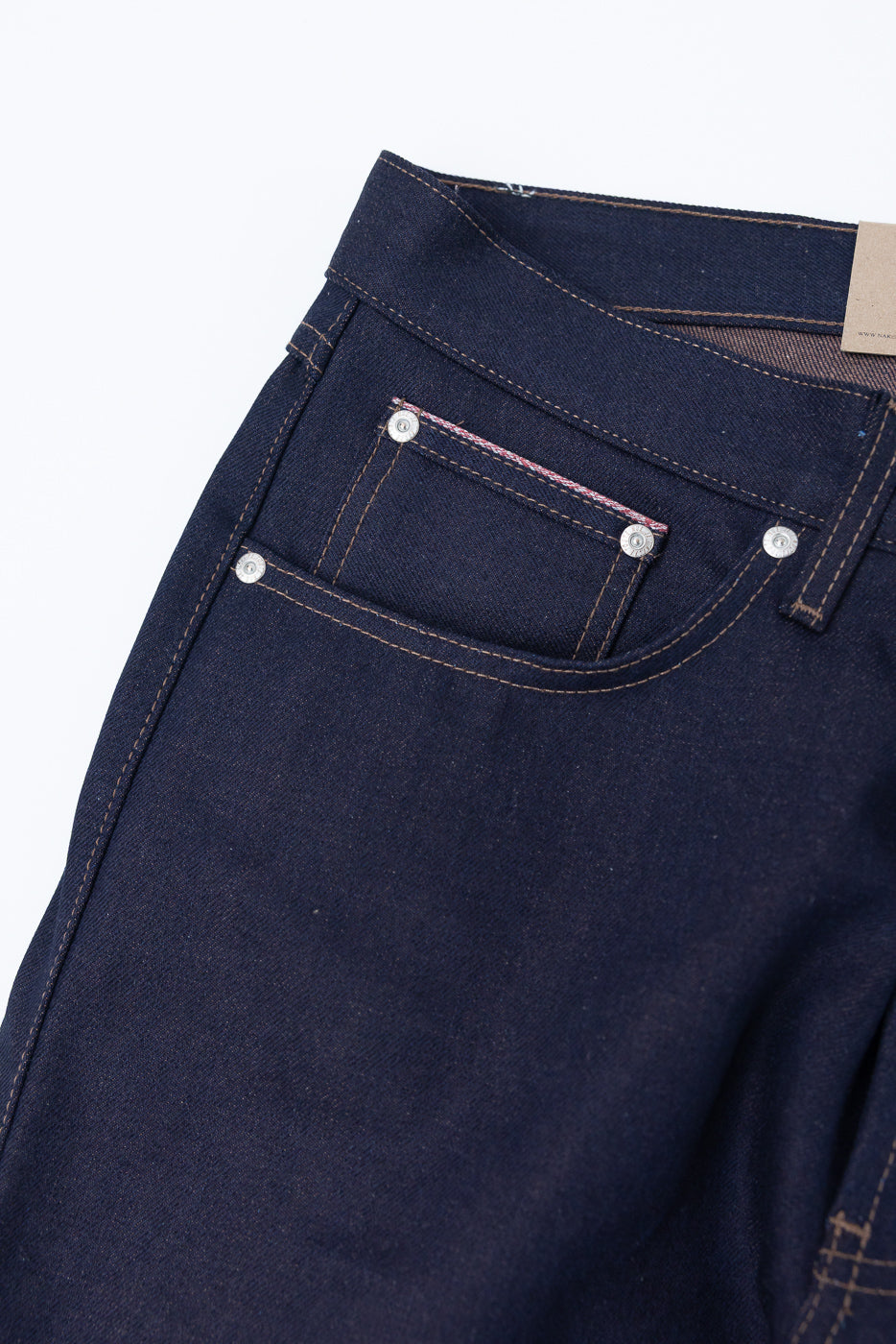 Close-up of men's raw selvedge denim jeans, front left waist and pocket, showing stitching and rivets.