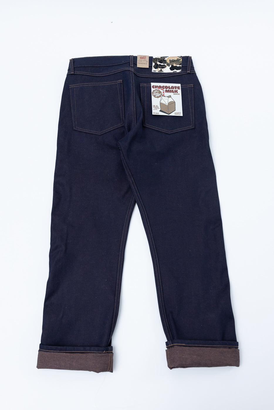 Flat lay of men's raw selvedge jeans, back view, showing rear pockets, cuffed hems, and tags.