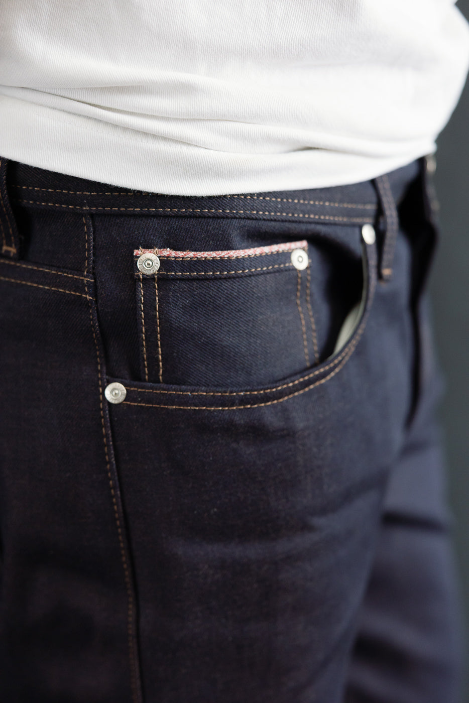 Close-up of front right pocket and selvedge detailing on men's raw denim jeans, worn by male model 5'9