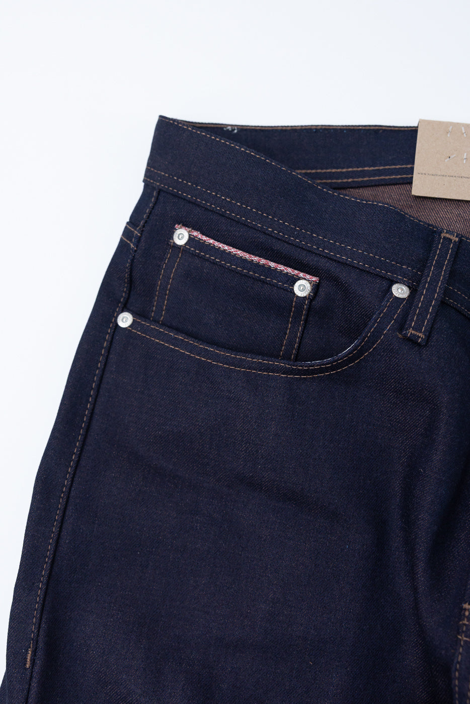 Close-up of front right waist and pocket on dark selvedge denim jeans, showing stitching and coin pocket details.