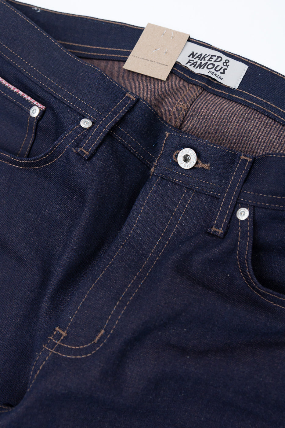 Close-up of front waistband and pockets on dark indigo selvedge denim jeans, showing button, stitching, and fabric texture.